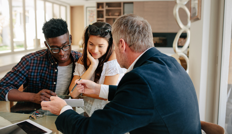 Real estate agent showing detail of lease agreement to interracial couple. Estate broker explaining lease agreement or purchase contract to couple in a new house.