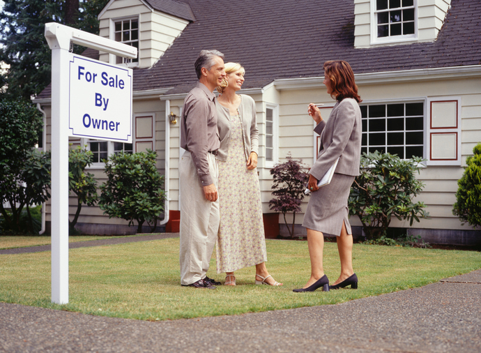 Couple talking to real estate agent on front lawn of house for sale