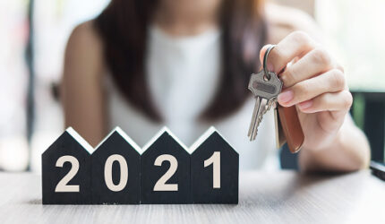 Young Businesswoman hands holding key and 2021 Happy New Year with house model on table office. New House, Financial, Property insurance, real estate, savings and New Year Resolution concepts